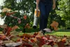 A person is using a leaf blower to clear fallen leaves from a lawn. Produktbild-Vorschau