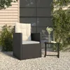A dark rattan garden chair with beige cushions sits on a gravel patio next to a small side table with a vase of flowers. Voir les images du produit