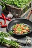 A frying pan with cooked shrimp and ingredients for cooking on a wooden table. Voir les images du produit