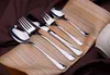 A set of shiny silverware is arranged on a striped cloth, with a brown fabric background. Anteprima dell’immagine prodotto