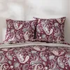 A close-up view of a bed with paisley patterned pillows and a comforter. Produktbild-Vorschau