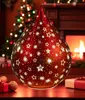 A red, star-patterned LED decorative drop light sits on a wooden surface in front of a fireplace and a Christmas tree. Produktbild-Vorschau