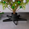 A close-up shot of a Christmas tree stand with a small tree inside, decorated with green and silver ornaments. Náhled obrázku produktu