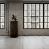 A wooden pedestal with a sculpture on top, placed in a room with brick walls and large windows. Anteprima dell’immagine prodotto