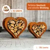 Two heart-shaped metal log holders filled with firewood, displayed on a light-colored floor with a wooden plank background. Produktbild-Vorschau