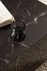 A close-up of a black marble-look coffee table with a glass of water and an open book. Náhľad obrázku produktu
