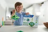 A young boy is holding a Geomag construction and smiling, with the product box on the table. Náhled obrázku produktu