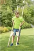 A young boy is standing in a grassy yard with trees in the background, holding a pair of wooden stilts. Anteprima dell’immagine prodotto