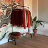 A clothing rack with several garments and shoes on a shelf, placed in a room with a large tapestry and a potted plant. Náhľad obrázku produktu