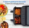 A dual-basket air fryer with food in the baskets and on a plate, set against a white wooden background. Produktbild-Vorschau