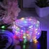 A coiled string of colorful LED lights with a blurred background of flowers and a potted plant. Produktbild-Vorschau