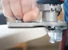 A close-up shot of a hand using a router on the edge of a white surface. Produktbild-Vorschau