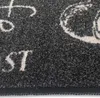 A close-up view of a textured black rug with white lettering. Anteprima dell’immagine prodotto