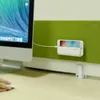 A smartphone charging holder is attached to a cubicle wall next to a computer monitor. A hand is visible on a mouse in the foreground. Produktbild-Vorschau