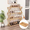 A wooden shoe rack filled with various shoes, placed near a potted plant and a wall. Produktbild-Vorschau