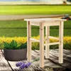 A wooden stool sits on a rustic wooden surface with a potted plant and lavender sprigs in front of a blurred field background. Voir les images du produit