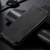 A black flip-style phone case with brown stitching and brass-colored rivets is displayed on a dark, textured surface, with a black smartwatch in the background. Produktbild-Vorschau