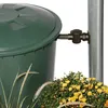 A close-up of a green rain barrel with a brown spigot attached to a metal pole, surrounded by plants. Náhled obrázku produktu