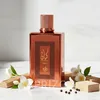 A bottle of perfume is displayed with decorative elements like wood, flowers, and peppercorns. Anteprima dell’immagine prodotto