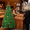 A Christmas tree decorated with ornaments stands in front of a bakery counter where a baker is serving a customer. Voir les images du produit