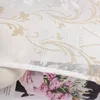 A close-up of a white fabric with a gold floral pattern, partially covering a magazine spread featuring a bouquet of pink tulips and a person's hands. Produktbild-Vorschau