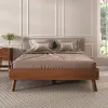 A bed with wooden frame and brown bedding is shown in a room with decorative wall panels and a window with greenery outside. Produktbild-Vorschau