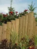 A wooden palisade fence bordering a garden with flowers and greenery. Produktbild-Vorschau