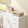A white cabinet with drawers and doors, topped with books and a wooden radio. Náhled obrázku produktu