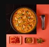 A wok pan filled with shrimp curry is placed on a black induction stovetop, with a detachable handle and small dishes of ingredients on a red surface. Voir les images du produit