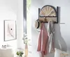 A wooden and woven wall-mounted coat rack with a hat, jacket, and scarf hanging on it, placed in a hallway with a framed picture on the wall. Produktbild-Vorschau