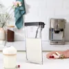 A close-up of a milk container for a coffee machine, with a latte in a glass in the foreground and a coffee machine in the background. Anteprima dell’immagine prodotto