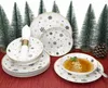 A Christmas-themed dinnerware set with snowflake and star patterns, arranged with miniature Christmas trees and a pinecone. Podgląd zdjęcia produktu