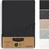 A fitted sheet is shown in black, with a cardboard tag attached. Several other fitted sheets in different colors are displayed vertically on the right side of the image. Produktbild-Vorschau
