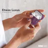 Hands holding an open purple case with white earbuds inside. Produktbild-Vorschau