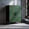 A green metal cabinet with two doors and handles stands on metal legs in a room with concrete walls and floor. Náhľad obrázku produktu