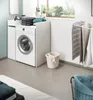 A laundry room with a washing machine, storage units, and laundry accessories. Produktbild-Vorschau