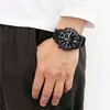 A person wearing a white t-shirt and dark pants, with a black watch on their wrist. Voir les images du produit