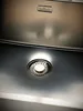 A close-up view of a stainless steel sink drain with a brand logo above it. Produktbild-Vorschau