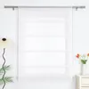 A white sheer Roman blind hangs on a window, with a floor lamp and a vase of tulips on the right. Produktbild-Vorschau