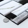 Nahaufnahme von abziehbaren Fliesen in Weißmarmor, Schwarz und Silber mit strukturierten Oberflächen, mit einer Münze als Größenvergleich Voir les images du produit