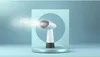 A white and gray handheld garment steamer is shown emitting steam, placed on a circular platform in front of a light blue background with a circular cutout. Voir les images du produit