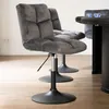 A close-up view of a gray upholstered chair with a metal base, placed on a wooden floor. Another similar chair and part of a table are visible in the background. Voir les images du produit