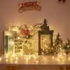 A festive Christmas display with string lights, books, flowers, a lantern with a deer figurine, and miniature Christmas trees. Produktbild-Vorschau
