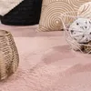A close-up view of a fluffy pink rug with decorative items on it. Produktbild-Vorschau