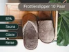 A pair of brown slippers are displayed in a wooden crate, with green leaves in the background. Text overlays indicate product features and categories. Produktbild-Vorschau