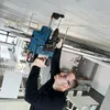 A man is using a Bosch rotary hammer drill to drill into a concrete ceiling in what appears to be an office or workshop environment. Produktbild-Vorschau
