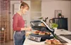 A woman is using a panini press in a kitchen. Podgląd zdjęcia produktu