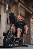 A man is exercising on a recumbent exercise bike in an outdoor urban setting. Produktbild-Vorschau