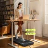 A woman is using a treadmill under a standing desk in a home office setting. Podgląd zdjęcia produktu
