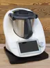 A white kitchen appliance with a black lid and handle, placed on a black base, against a wooden background. Produktbild-Vorschau